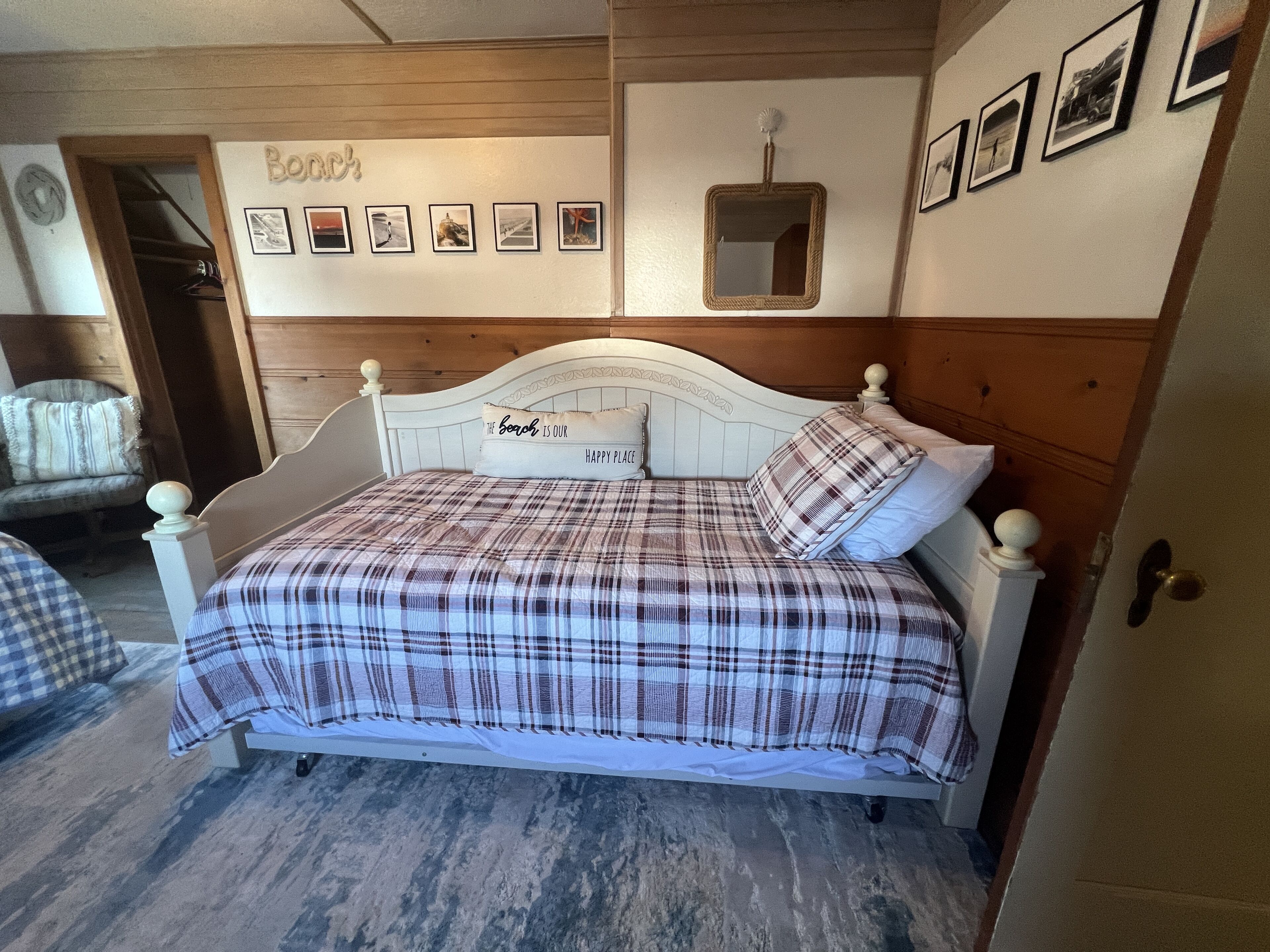 A bedroom with a bed, a wooden headboard, a wall with framed pictures, and a door.