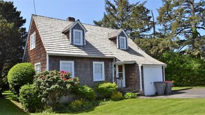 A two-story house with a gabled roof, a front porch, and a garage. - Simply Adorable Beach House - Sleeps 9, Near Beach & Town (Seaside)