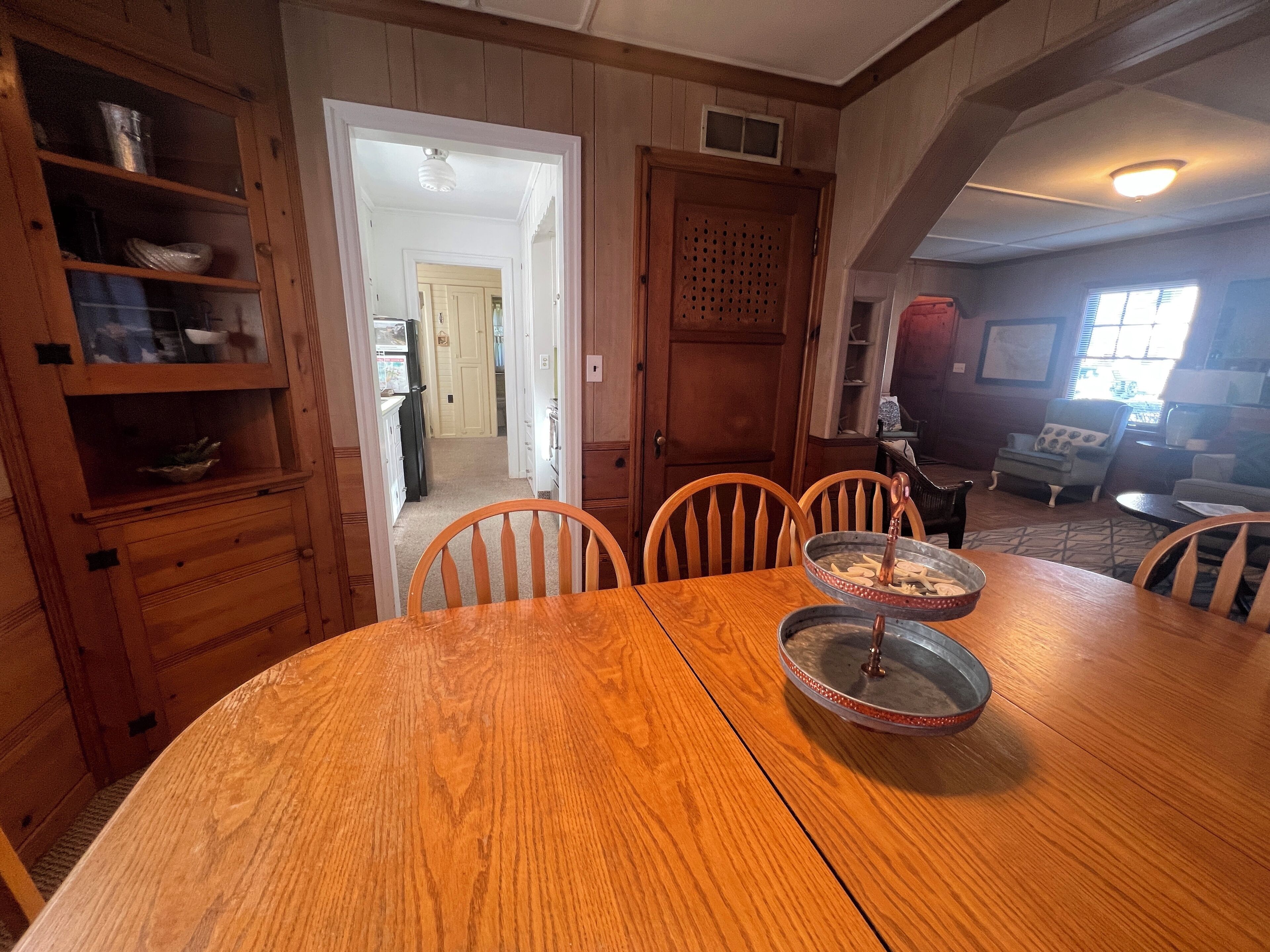 A dining area with a wooden table and chairs, a metal serving tray, and a wooden cabinet with shelves.