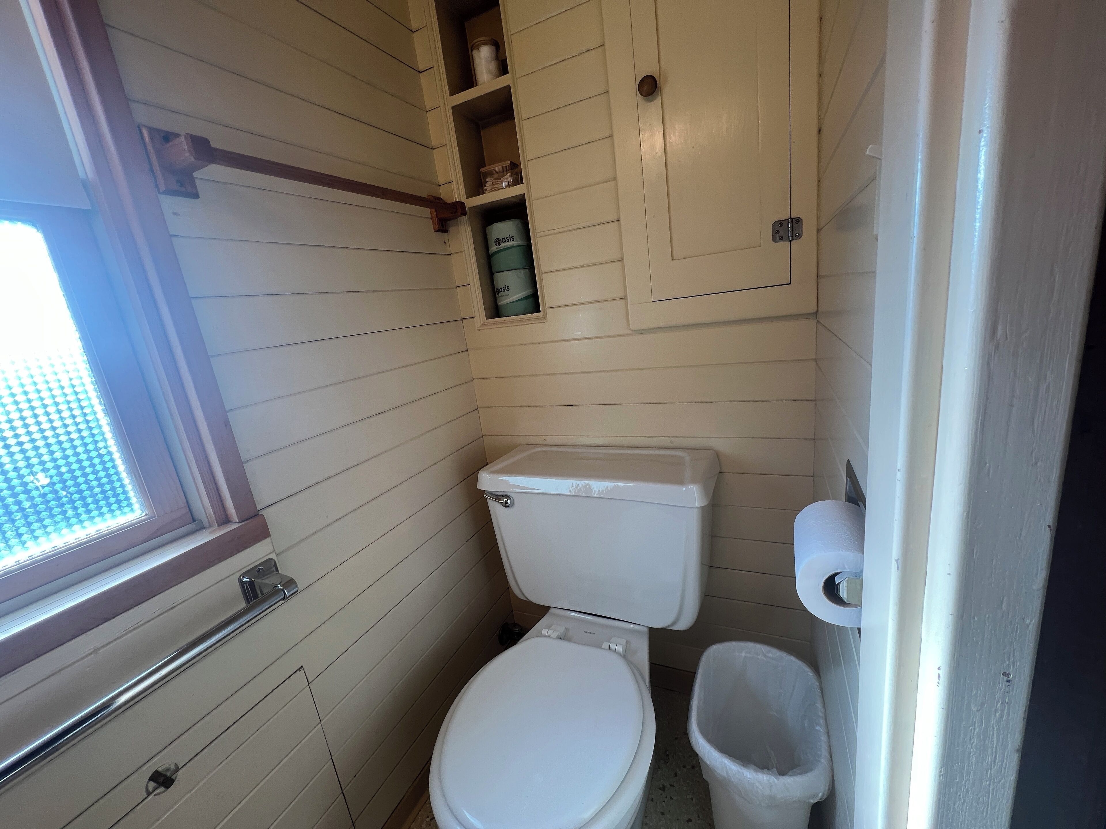 Ein kleines, kompaktes Badezimmer mit Toilette, Mülleimer und Fenster.