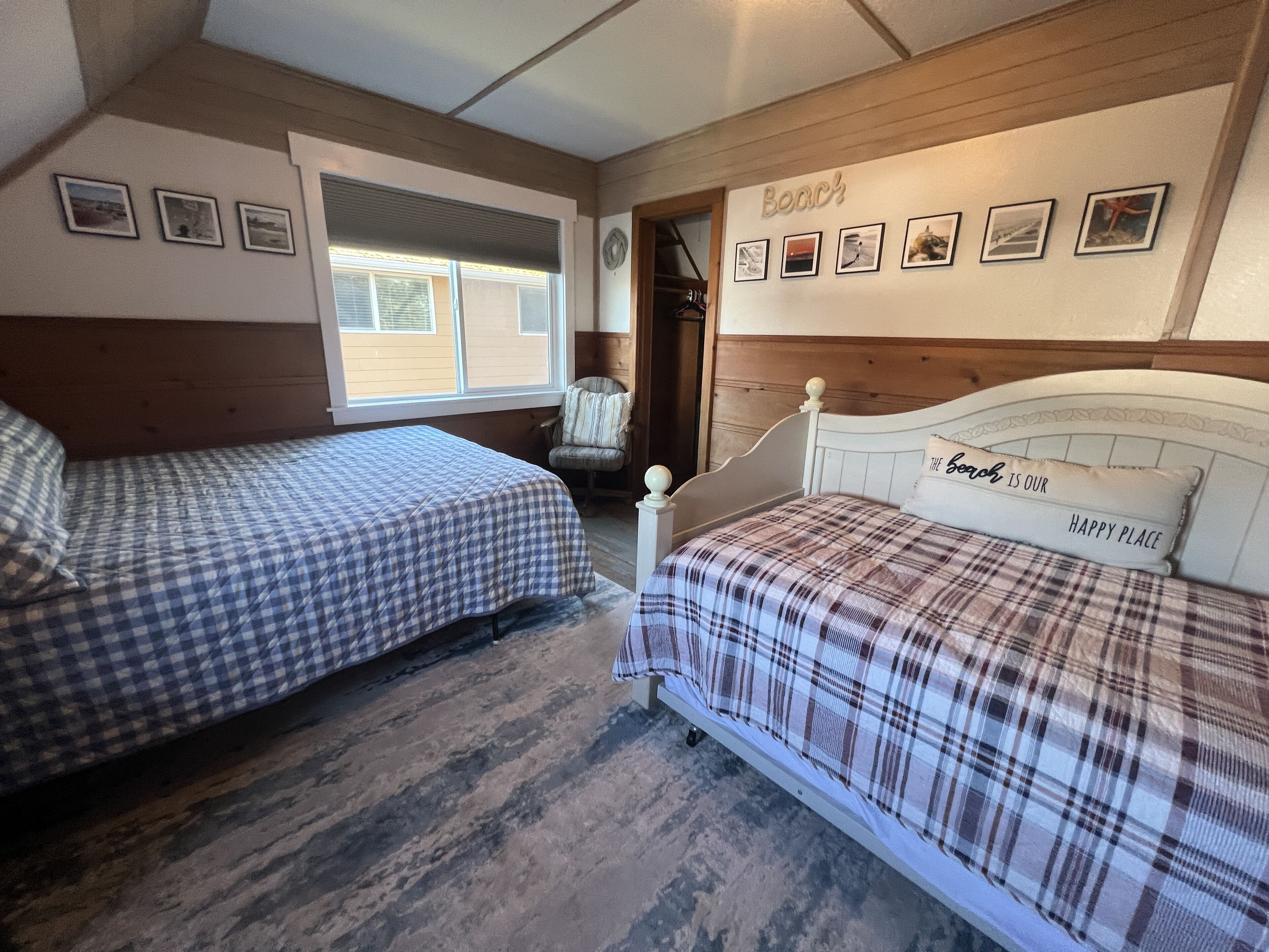 A bedroom with two beds, a window, and a wall with framed pictures and a 'Beach' sign.