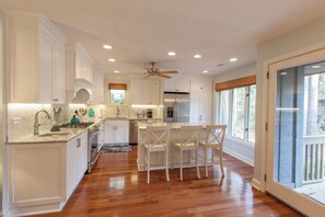 A modern kitchen with white cabinets, a stainless steel refrigerator, and a bar area with white chairs.
