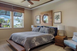 Une chambre à coucher comprenant un lit, une table de chevet, une chaise, un ventilateur de plafond et une fenêtre donnant sur des palmiers.