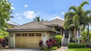 Una casa residenziale con un garage color beige, il numero 205 sulla porta e un prato curato con piante tropicali.