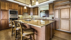Una cucina con mobili in legno, una grande isola con sgabelli da bar, elettrodomestici in acciaio inossidabile e illuminazione a sospensione.