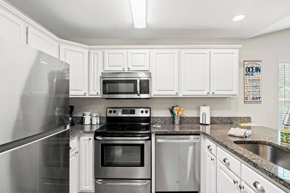 A modern kitchen with white cabinets, stainless steel appliances, granite countertops, and a built-in oven.