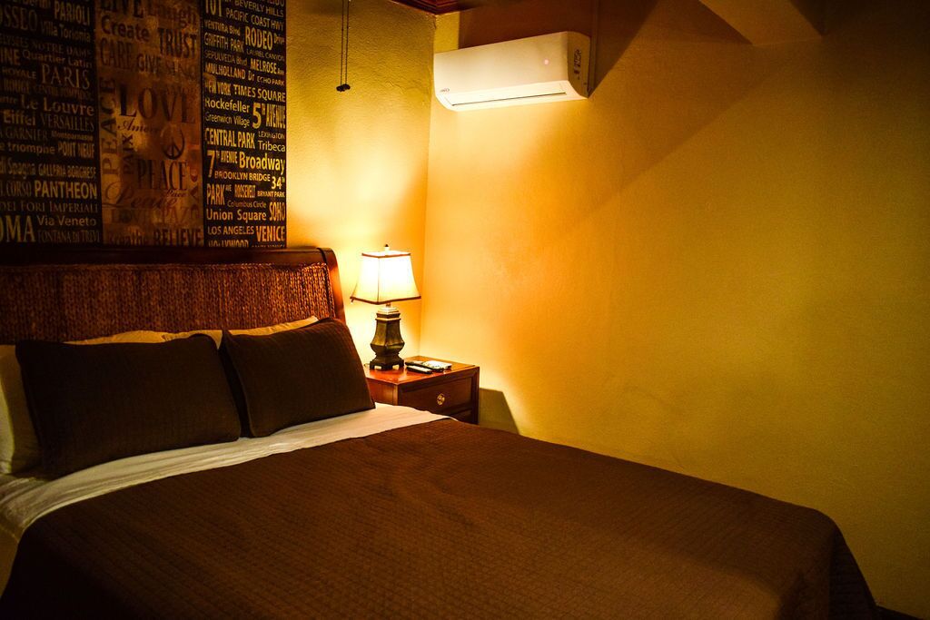 Une chambre d’hôtel avec un grand lit, une table de chevet avec une lampe et un mur sur lequel figurent différents noms de villes.