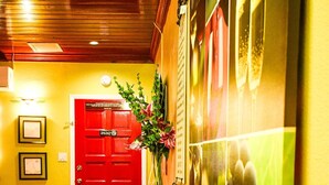 A hallway with a wooden floor, a red door, and a wall with framed pictures and a glass vase with flowers. - Brownstone Sea Beach (Nassau)