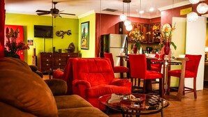 A living room with red furniture, a glass coffee table, and a kitchen area with wooden cabinets and a refrigerator. - Brownstone Sea Beach (Nassau)