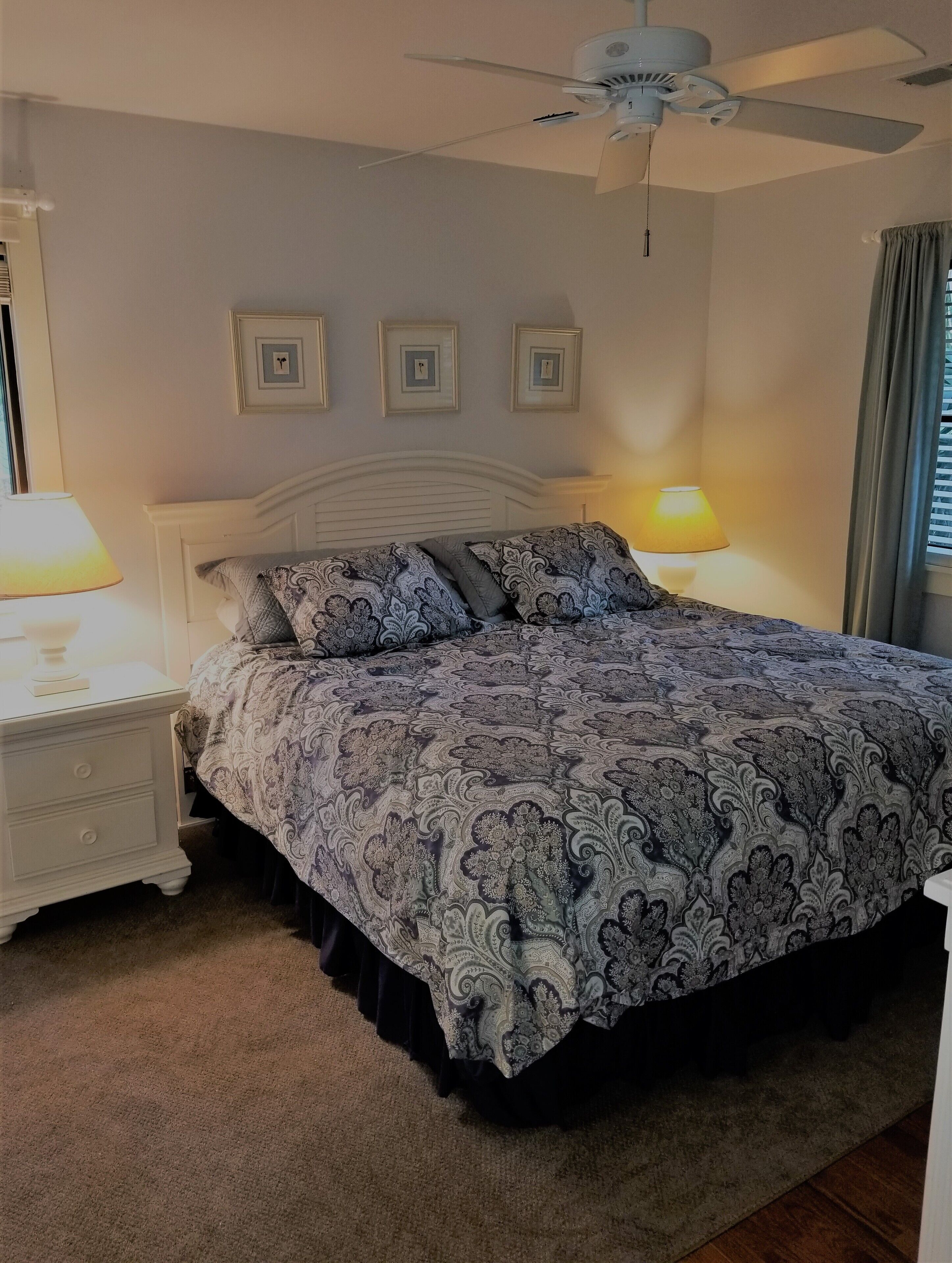 A bedroom with a bed, nightstands, a ceiling fan, and framed pictures on the wall.