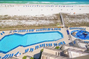 A beach resort with a large swimming pool, sun loungers, and a pier.