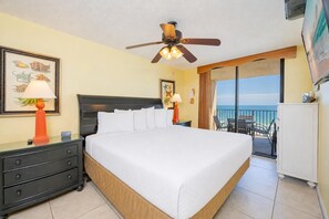 Habitación de hotel con cama, ventilador de techo, balcón con vista al océano y escritorio con lámpara.