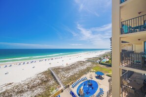 A beach view from a hotel balcony with a pool, lounge chairs, and a clear sky.