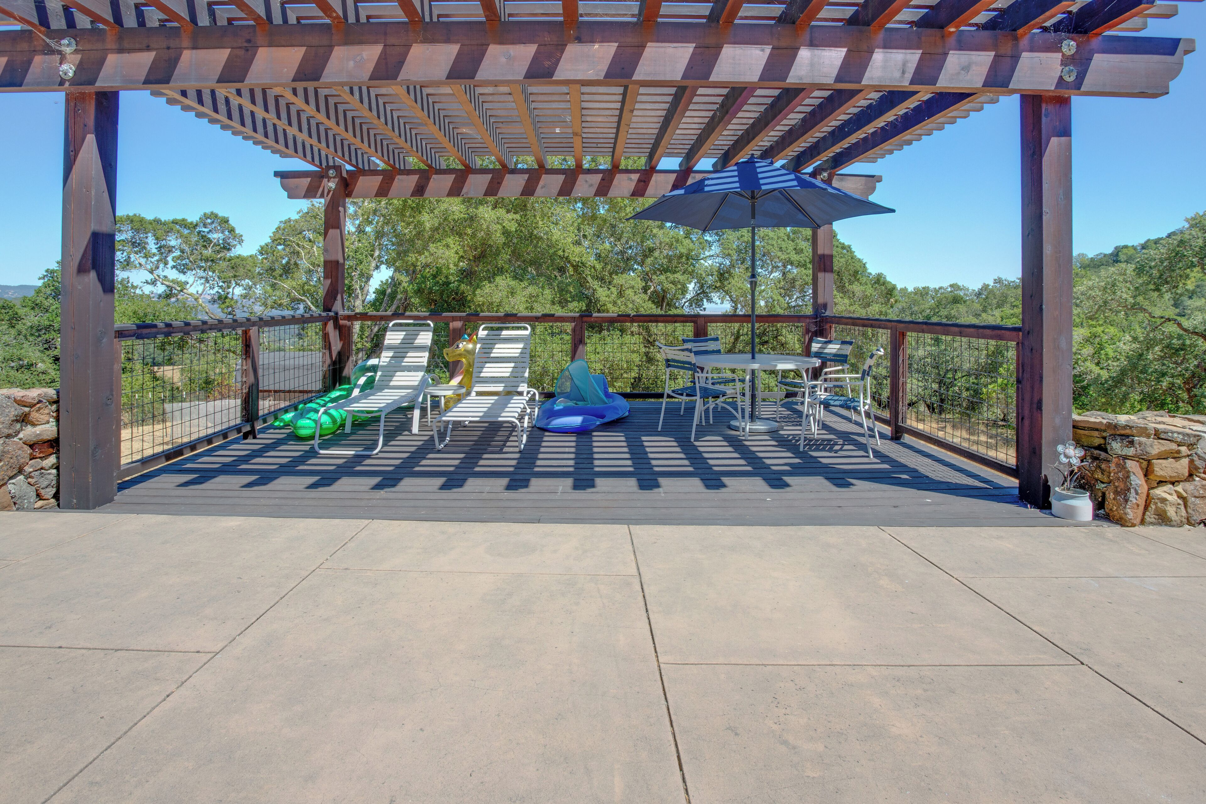 An outdoor patio with a pergola, seating area, and a table with chairs.