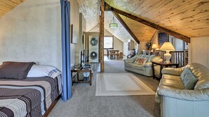 A spacious loft bedroom with a high ceiling, a large bed, a washing machine, and a cozy seating area with a sofa and armchairs.