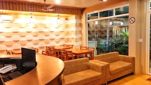 Zona de recepción con mostrador de madera, varias opciones de asientos incluyendo sofás y sillones, y un amplio ventanal con vistas al exterior.
