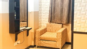 Pequeña habitación cerrada con un sillón estampado, un espejo y un estante en la pared con una botella.