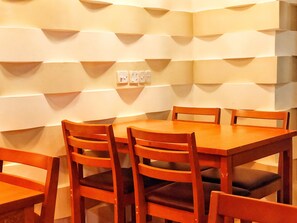 A dining area with a wooden table and chairs, a white textured wall, and a light switch panel. - Brize Inn (Hulhumalé)