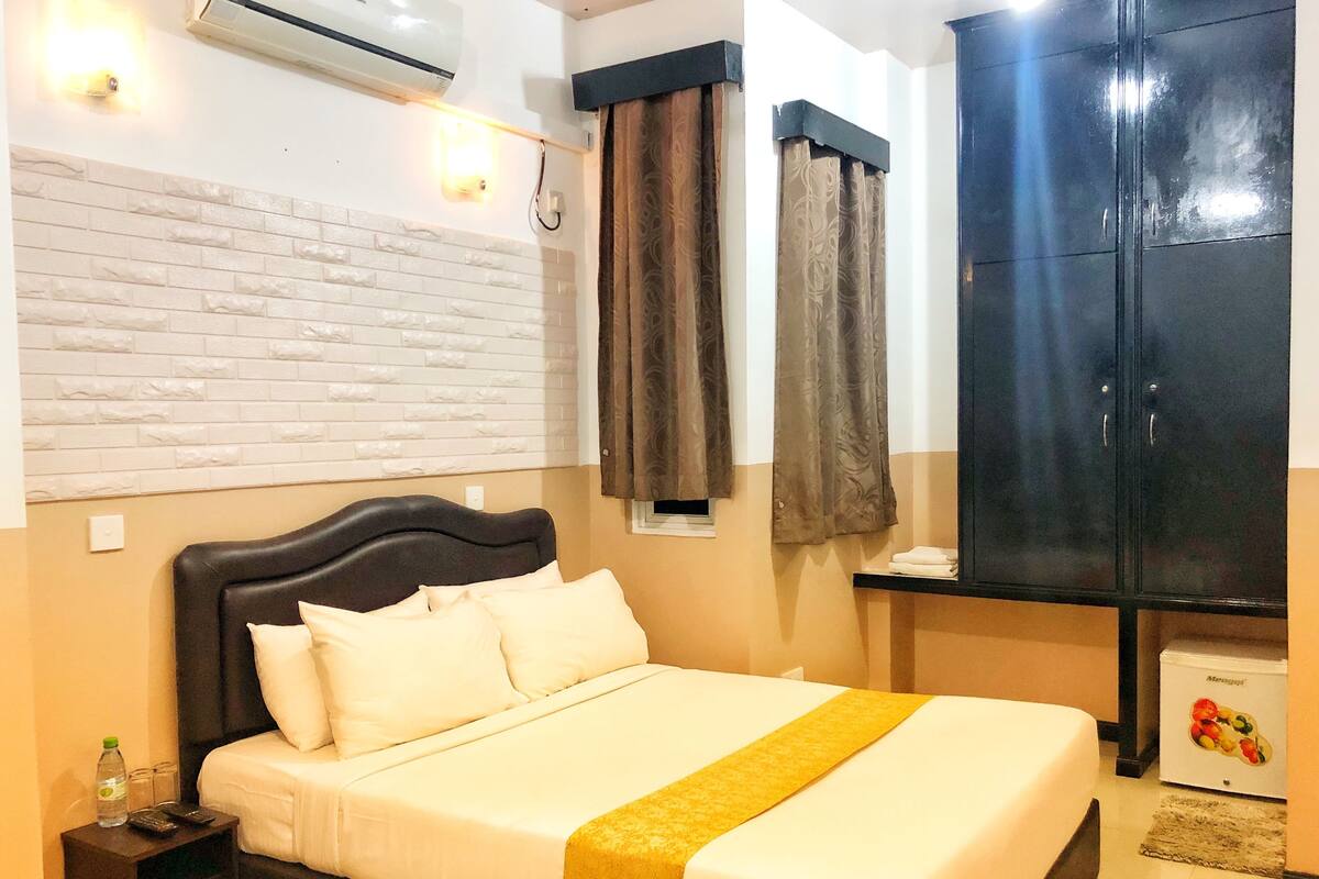 Une chambre d’hôtel comprenant un lit, une table de chevet, une armoire et un climatiseur fixé au mur.
