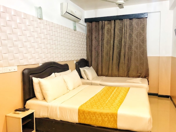 A double bed with a headboard, a bedside table with a phone and a remote control, and a window with curtains. - Brize Inn (Hulhumalé)