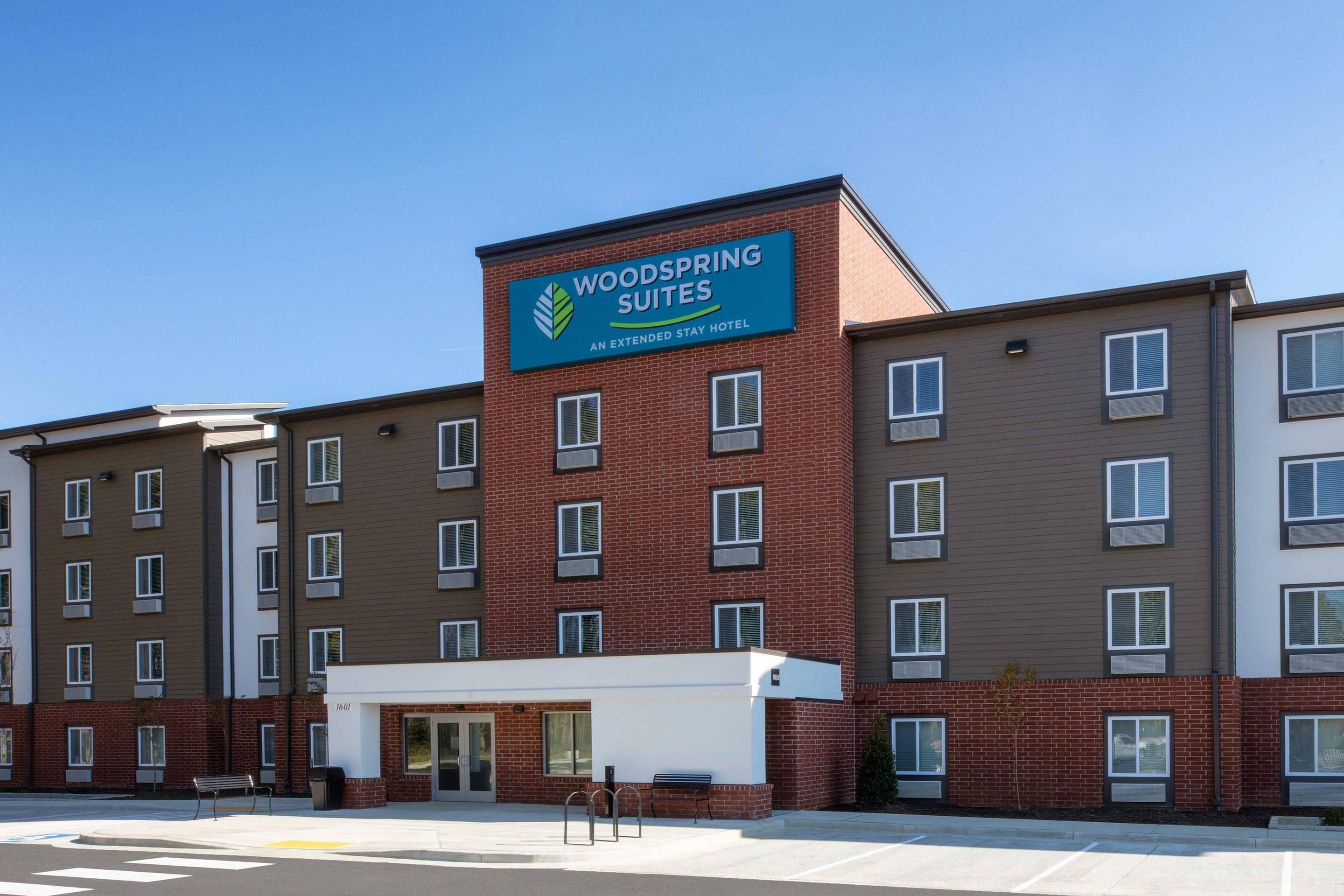 Ein mehrstöckiges Hotel mit einem gut sichtbaren Schild für 'Woodspring Suites', das es als Hotel für längere Aufenthalte kennzeichnet.