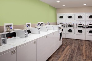 A commercial laundry facility with multiple washing machines and dryers, payment terminals, and a control panel. - WoodSpring Suites Washington DC East Arena Drive (Hyattsville)