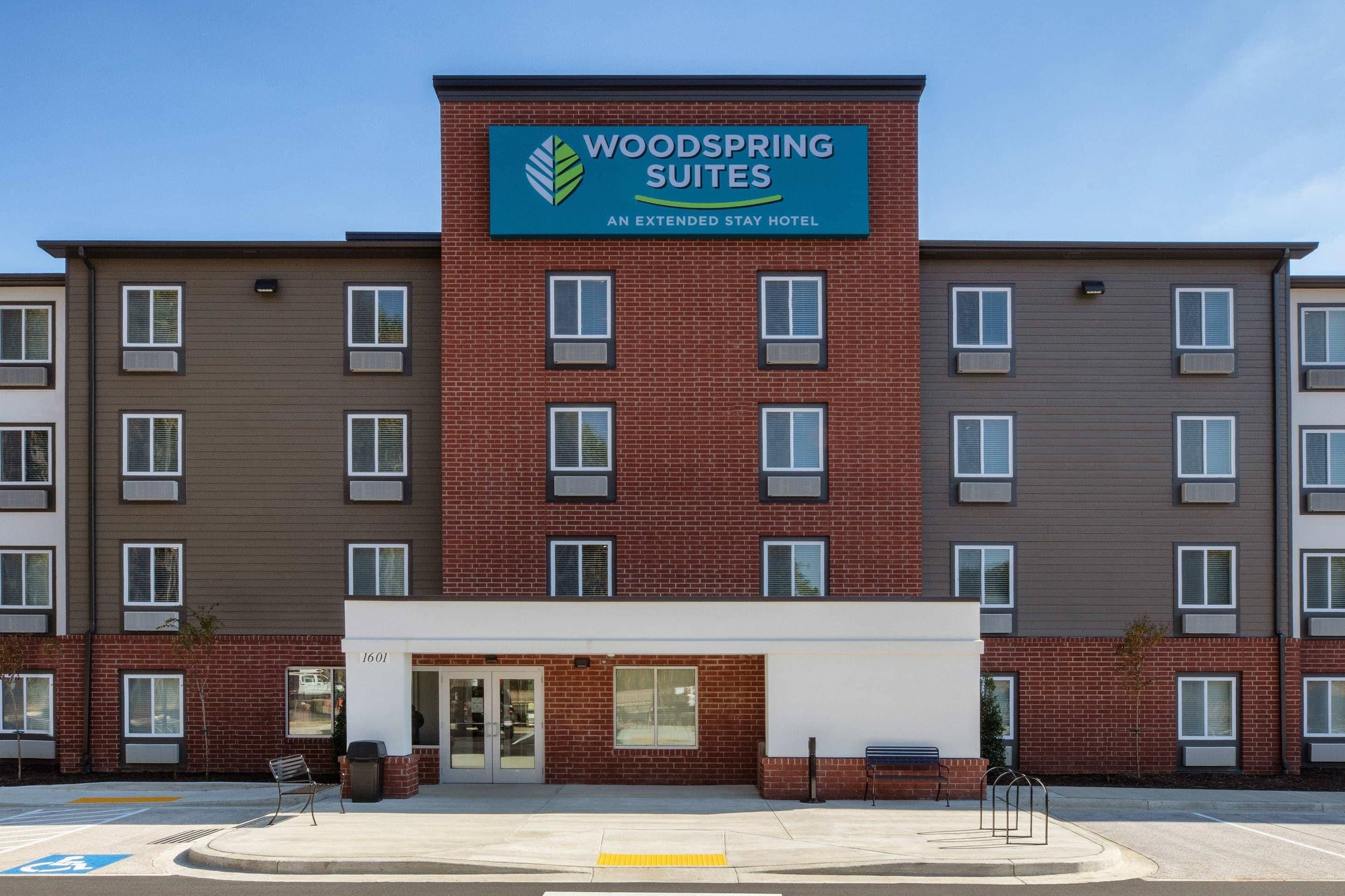 A multi-story hotel with a prominent sign for 'Woodspring Suites' indicating it is an extended stay hotel.
