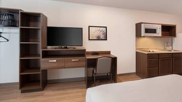 Habitación de hotel compacta con cama, escritorio con silla, televisor, cuadro enmarcado, microondas y armario empotrado.
