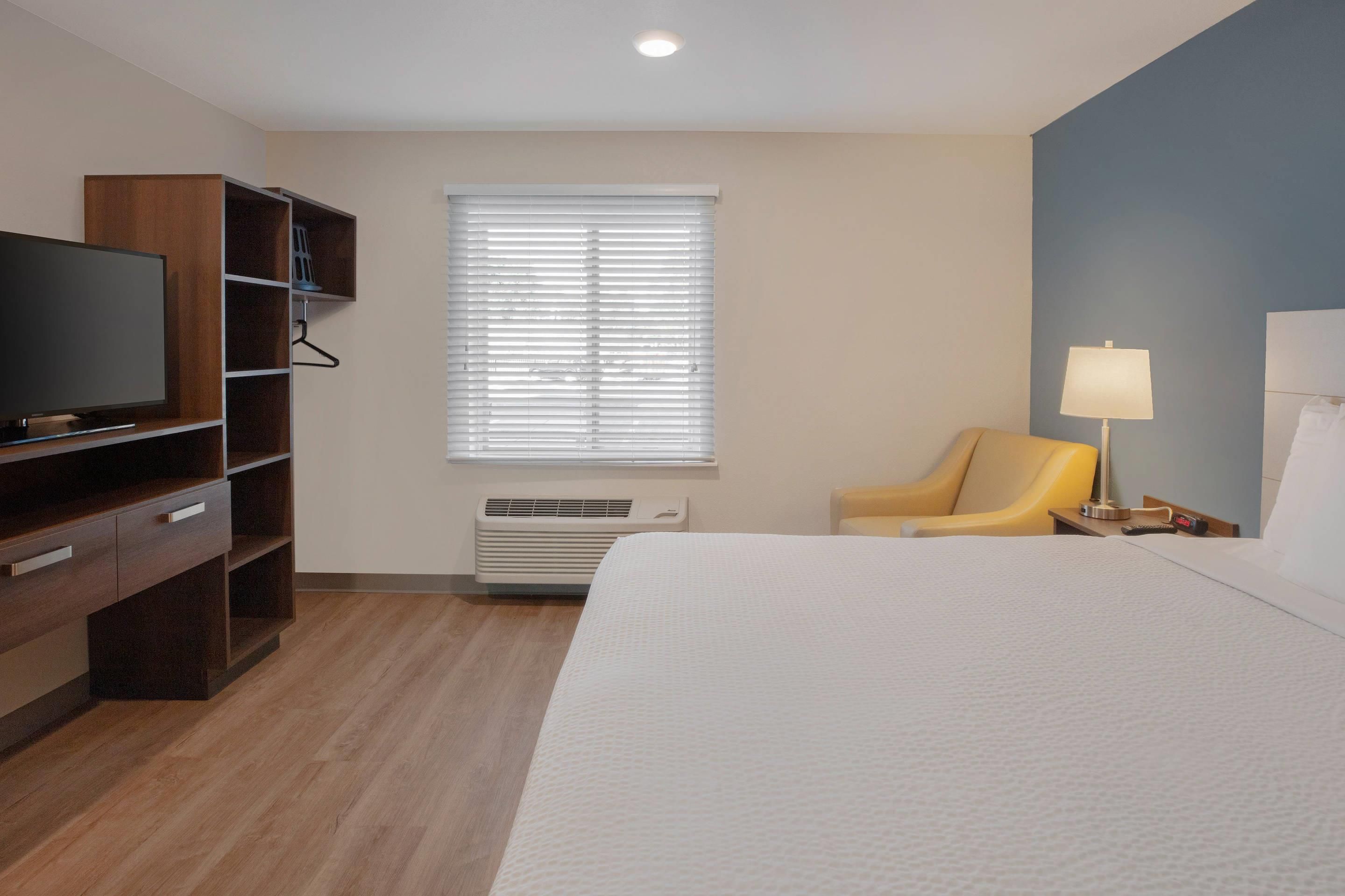A hotel room with a bed, a television, a chair, a lamp, and a window with blinds.