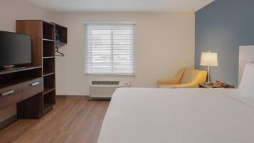 A hotel room with a bed, a television, a chair, a lamp, and a window with blinds.