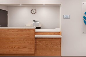 A reception area with a wooden desk, a clock, and a sign indicating check-in and check-out times. - WoodSpring Suites Washington DC East Arena Drive (Hyattsville)