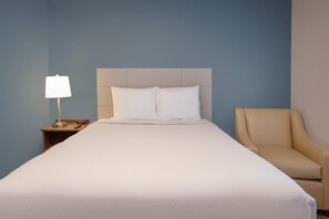 A hotel room with a bed, a nightstand with a lamp, a chair, and a wall clock. - WoodSpring Suites Washington DC East Arena Drive (Hyattsville)
