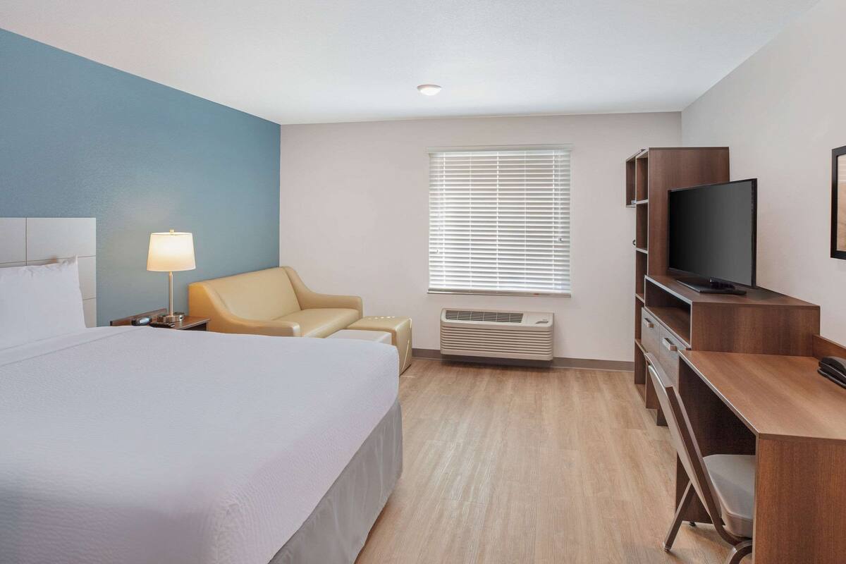 A hotel room with a bed, a desk, a chair, a television, and a window with blinds.