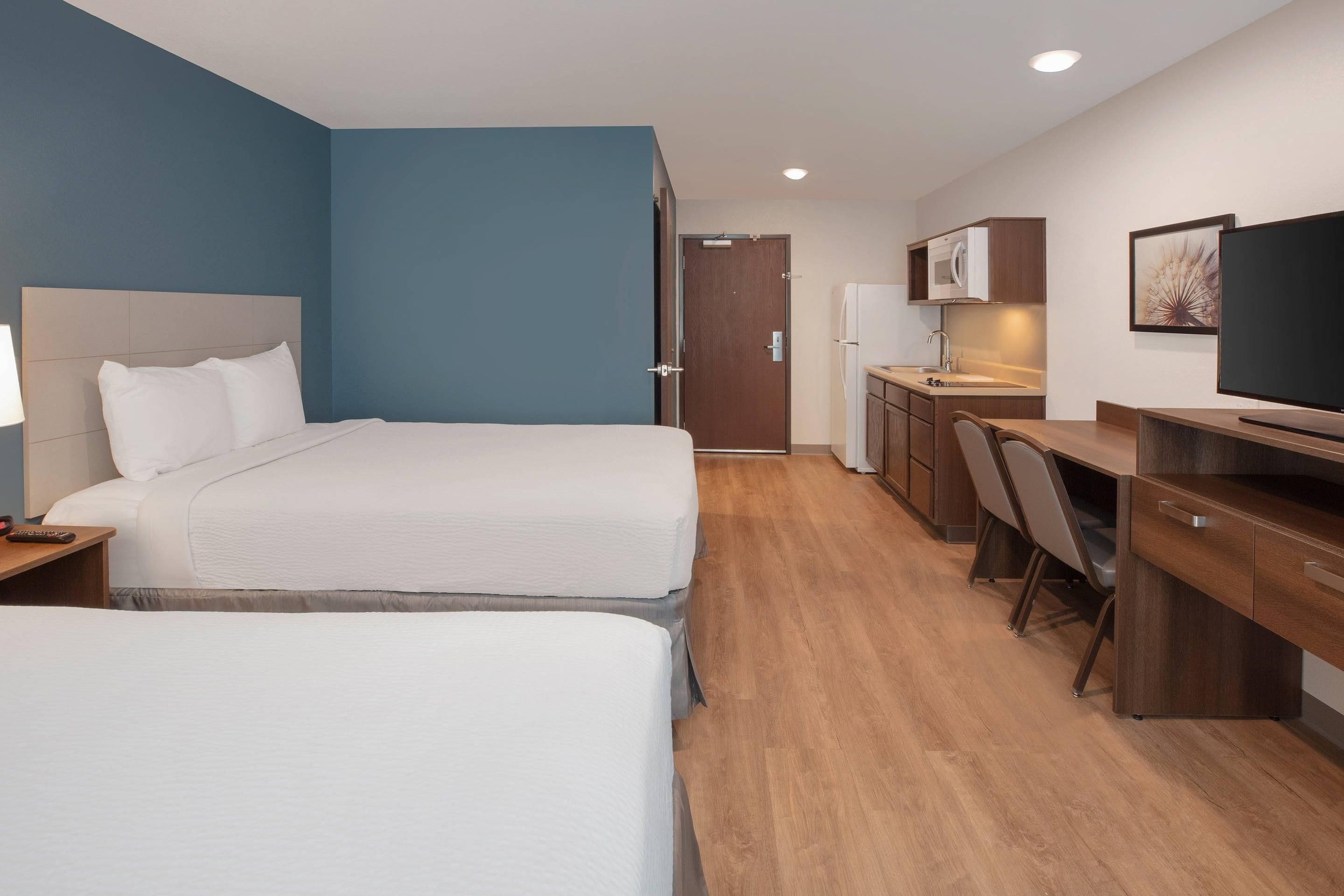 A hotel room with two beds, a desk, a chair, a television, and a kitchenette.