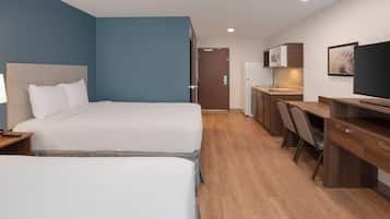 A hotel room with two beds, a desk, a chair, a television, and a kitchenette.