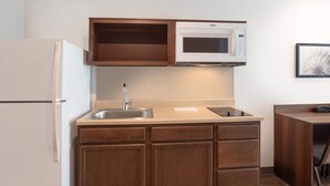 A compact kitchen with a built-in microwave, a refrigerator, and wooden cabinetry. - WoodSpring Suites Washington DC East Arena Drive (Hyattsville)