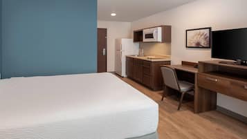 A hotel room with a bed, a desk, a chair, a television, a microwave, and a refrigerator.