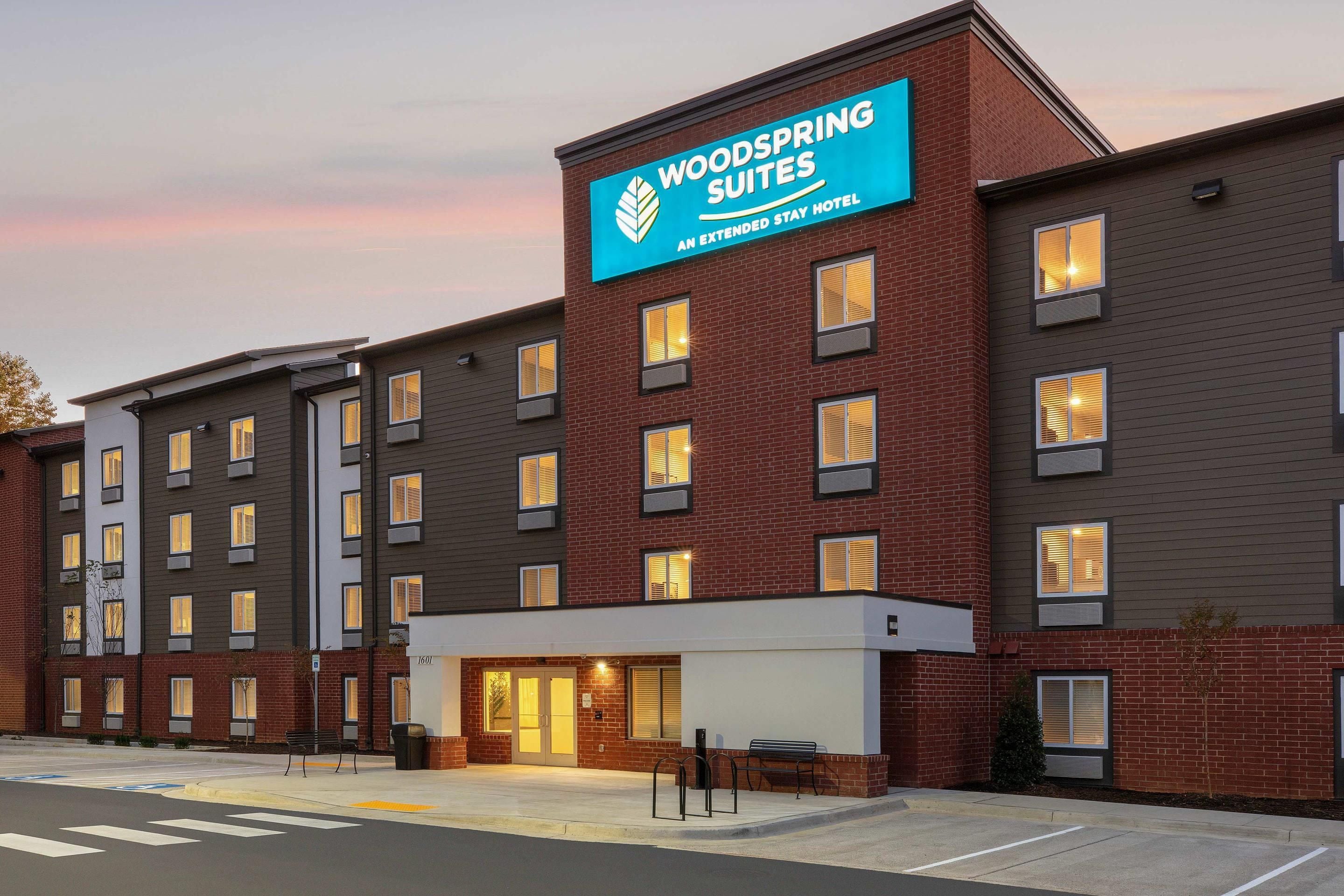 A multi-story hotel with a prominent sign for 'Woodspring Suites' indicating it is an extended stay hotel.