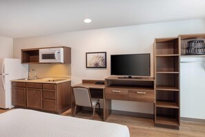 A compact hotel room with a kitchenette, a bed, a desk with a chair, and a TV. - WoodSpring Suites Washington DC East Arena Drive (Hyattsville)