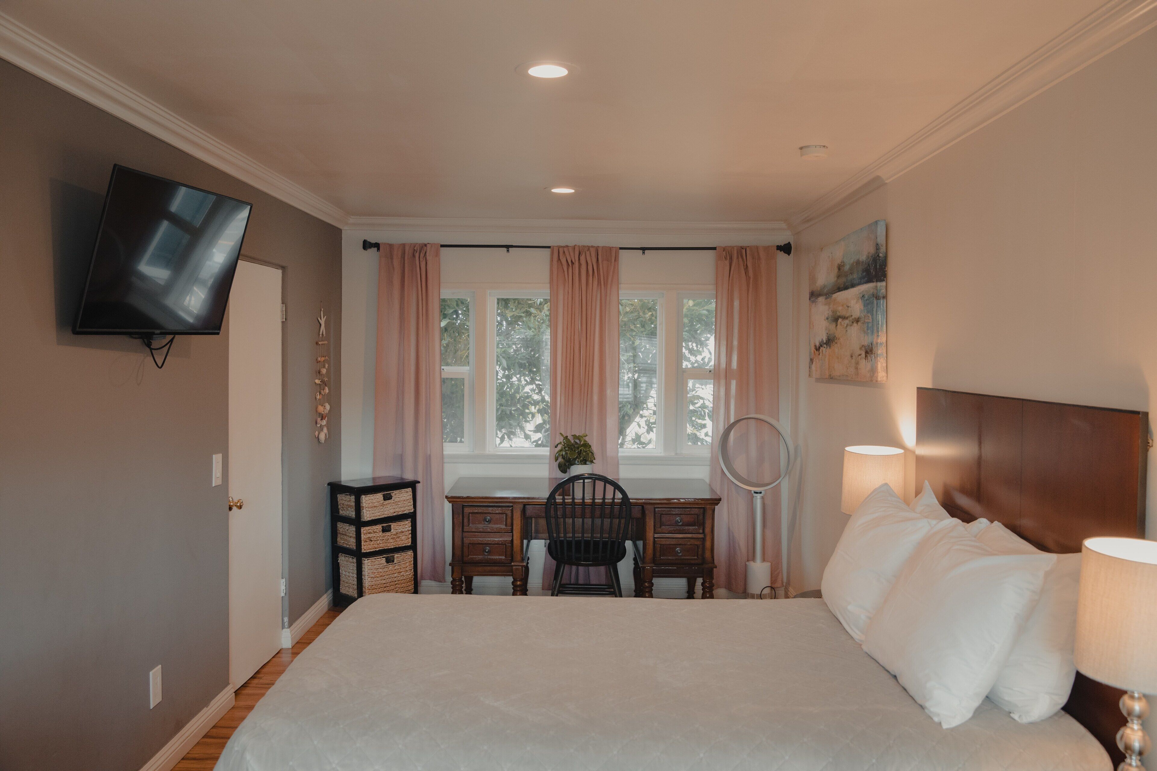 A bedroom with a bed, a desk, a chair, a television, and a window with curtains.