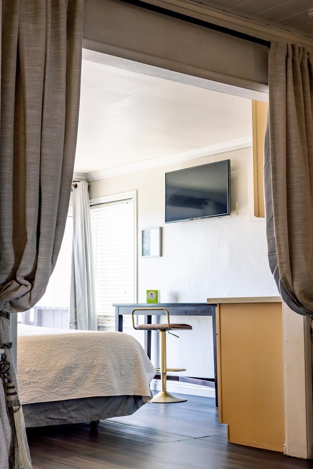 Habitación de hotel con cama, escritorio, silla, televisor y ventana con cortinas.