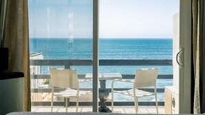 Un balcón con dos sillas de mimbre y una mesa, con vistas a un mar azul y despejado.