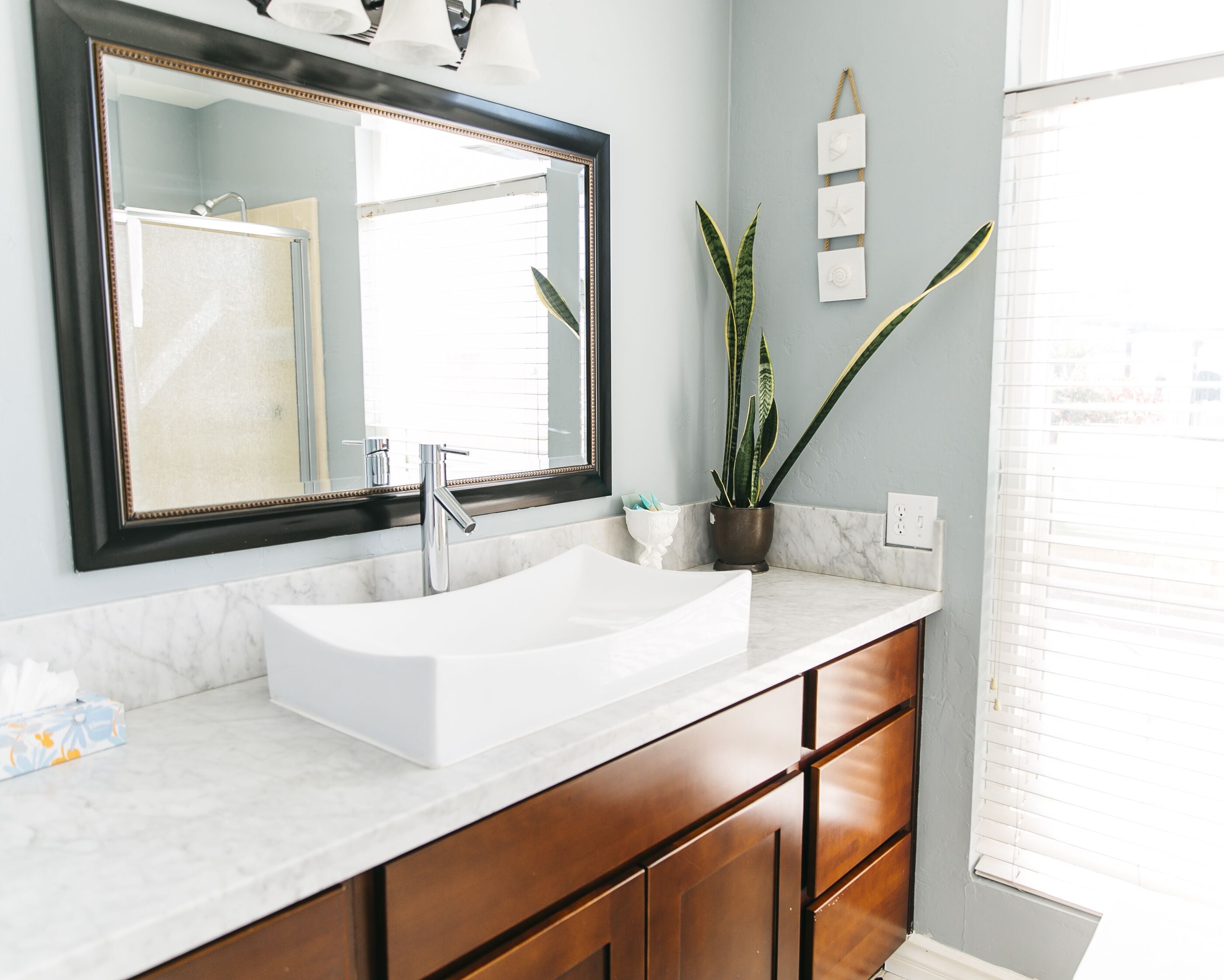 A bathroom with a white sink, a large mirror, wooden cabinets, and a potted plant.