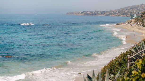 Vista costera con una playa arenosa, olas del océano y un pueblo lejano.