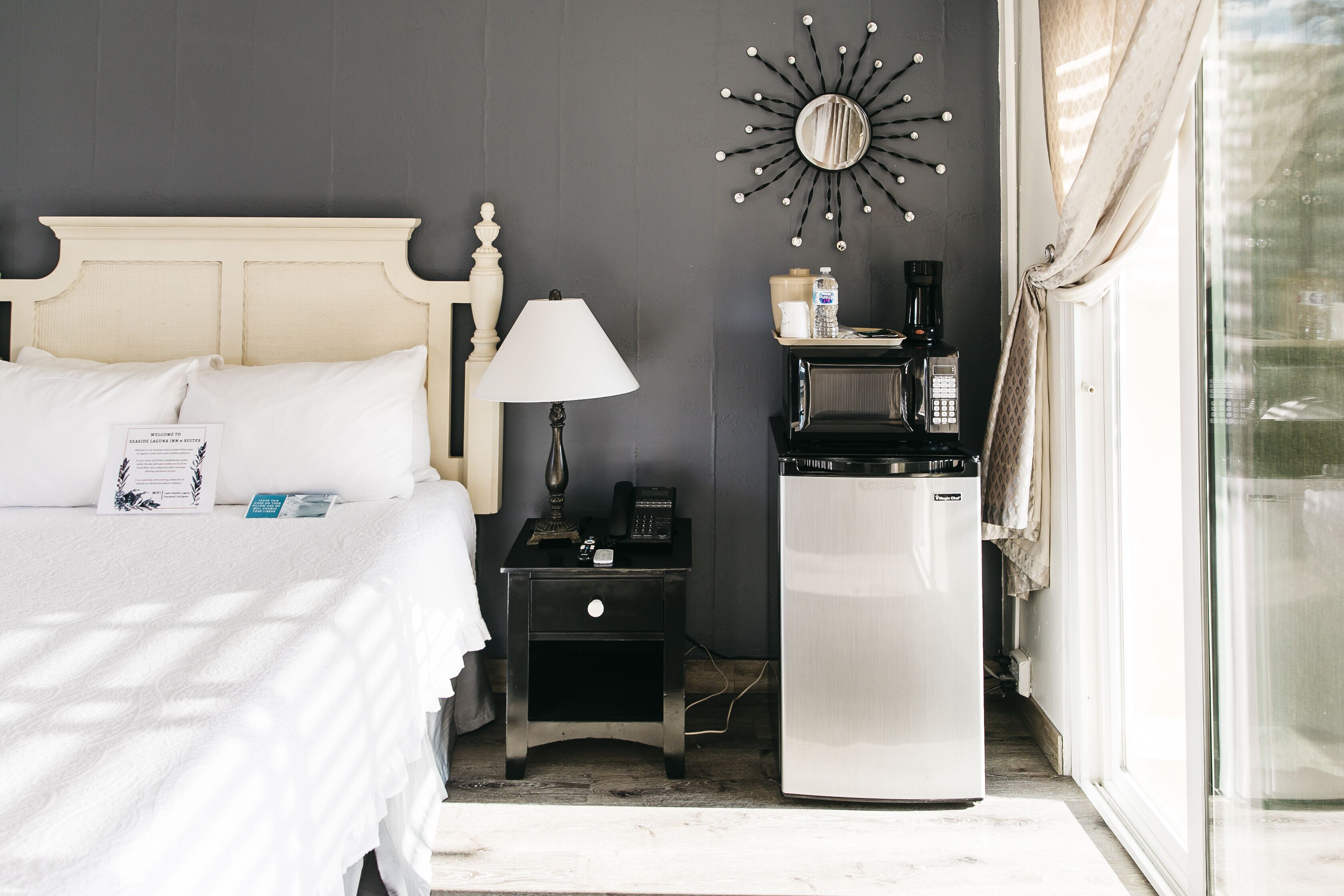 A hotel room with a bed, a nightstand, a coffee machine, and a mirror on the wall.