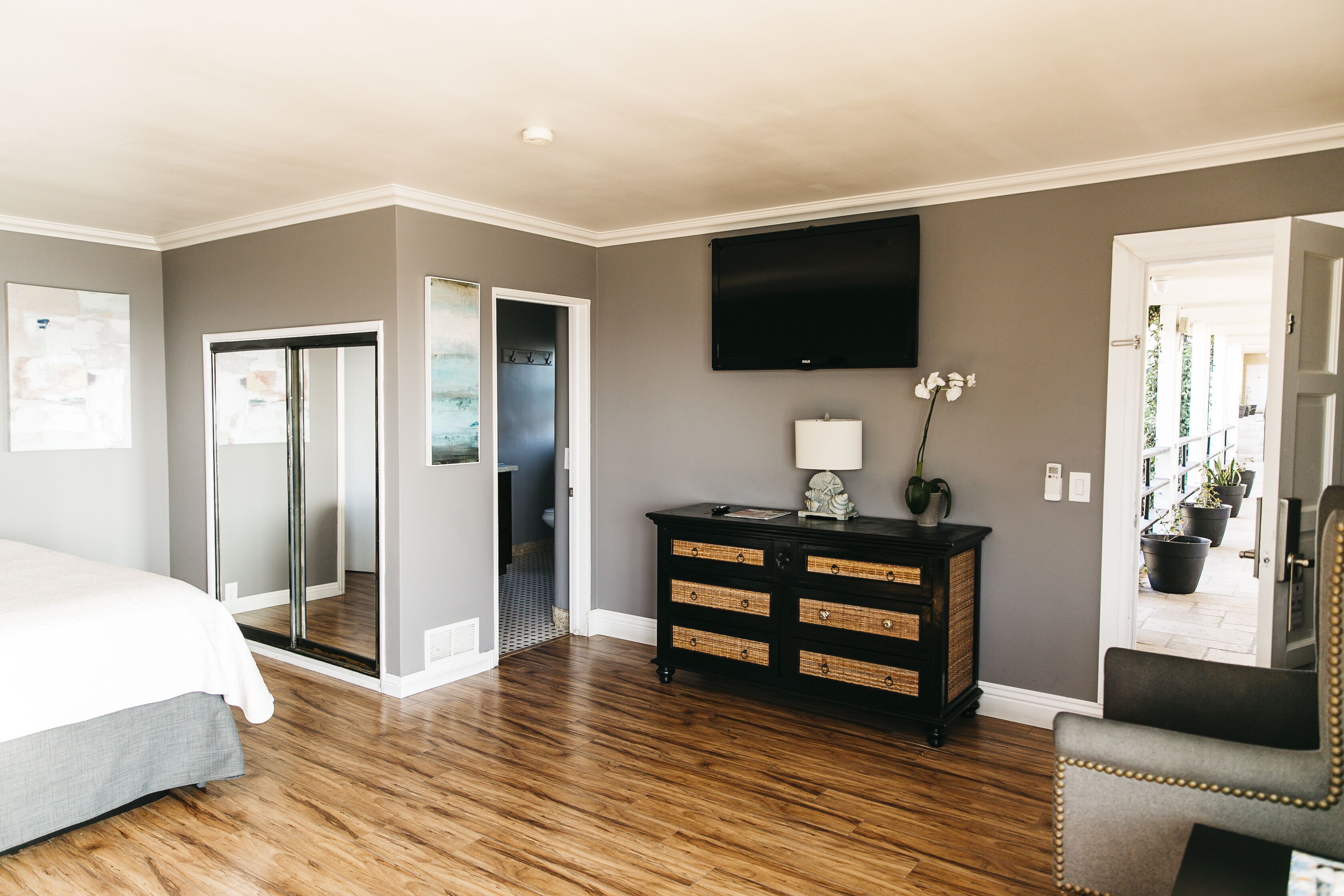 A bedroom with a bed, a dresser, a TV, and a door leading to a bathroom.