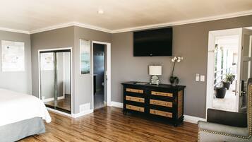 A bedroom with a bed, a dresser, a TV, and a door leading to a bathroom.