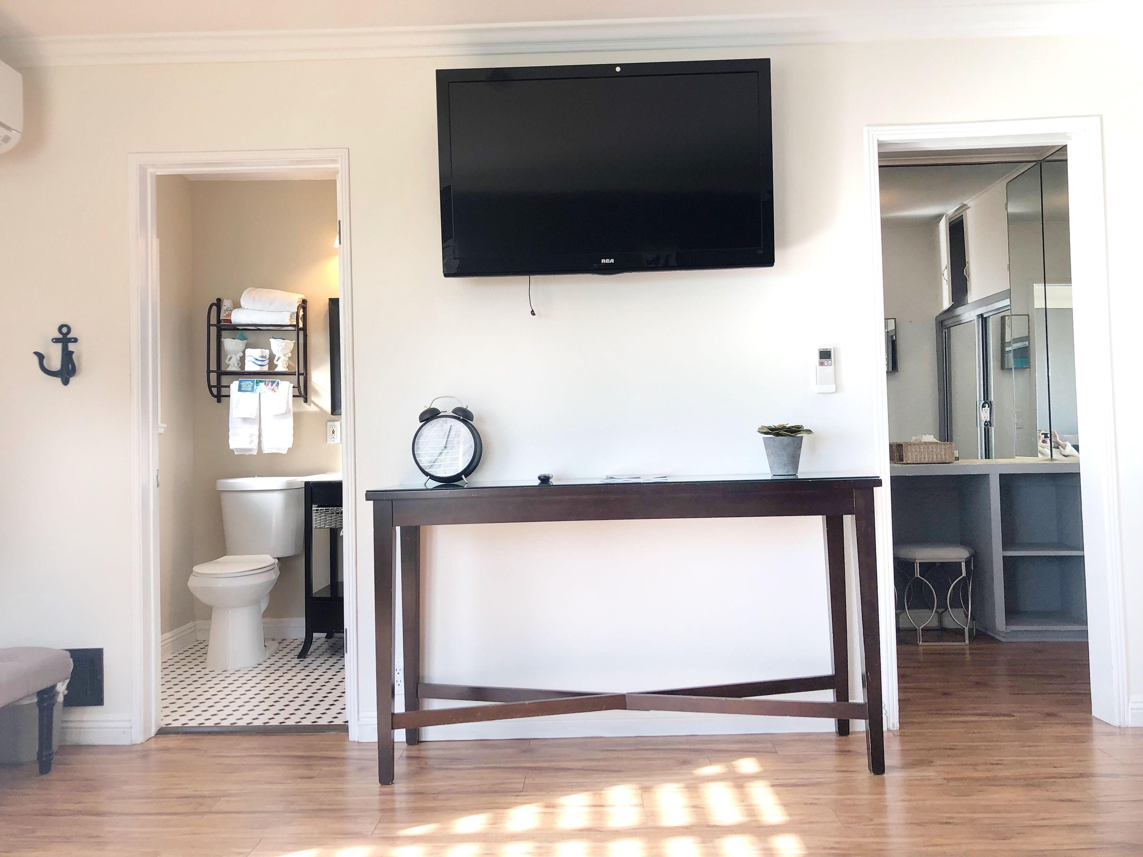 A room with a TV mounted on the wall, a wooden table, a clock, and a potted plant.