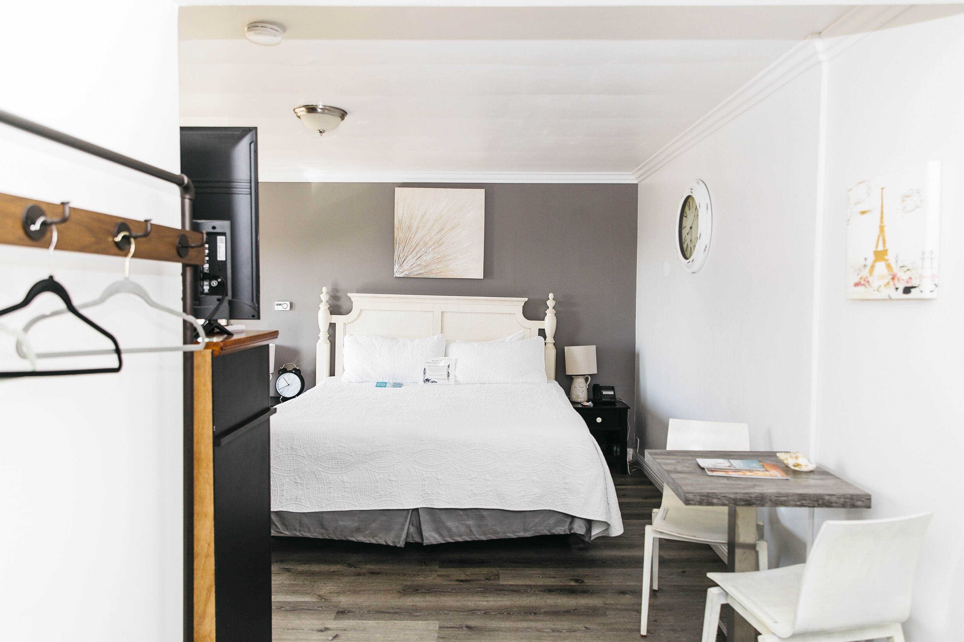 A hotel room with a bed, bedside table, chair, and a small desk with a chair.