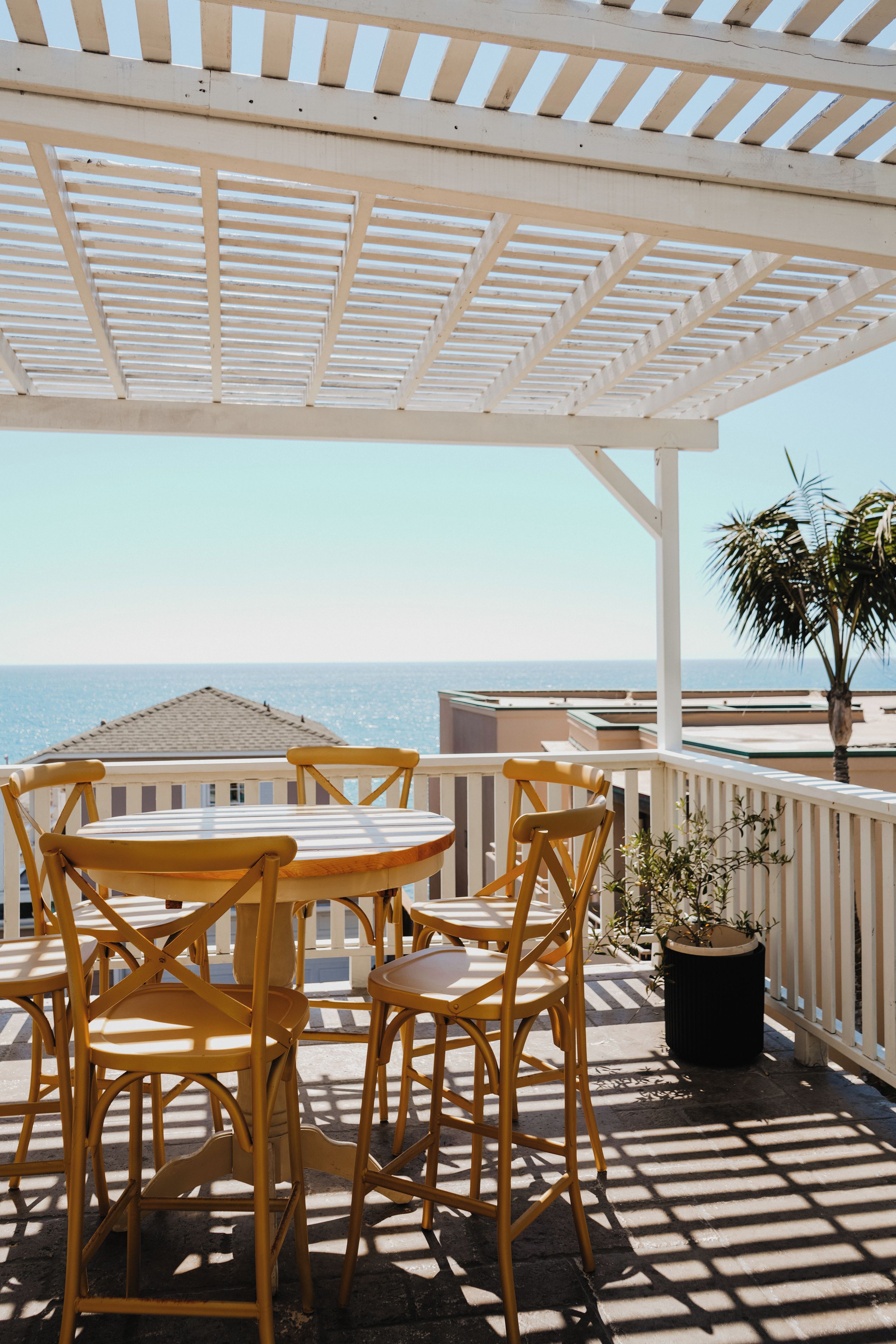 An outdoor patio with a table and chairs, a potted plant, and a view of the sea.